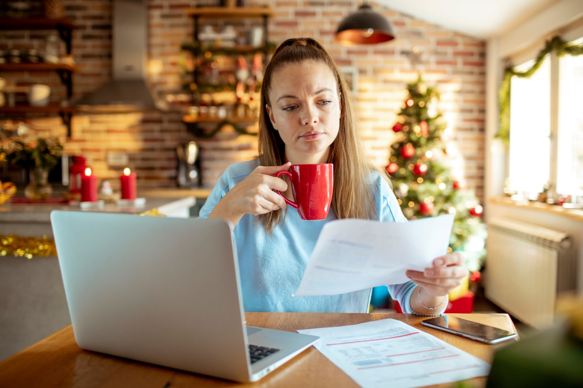 A person in their living room during the holidays holding a cup and looking at a paper